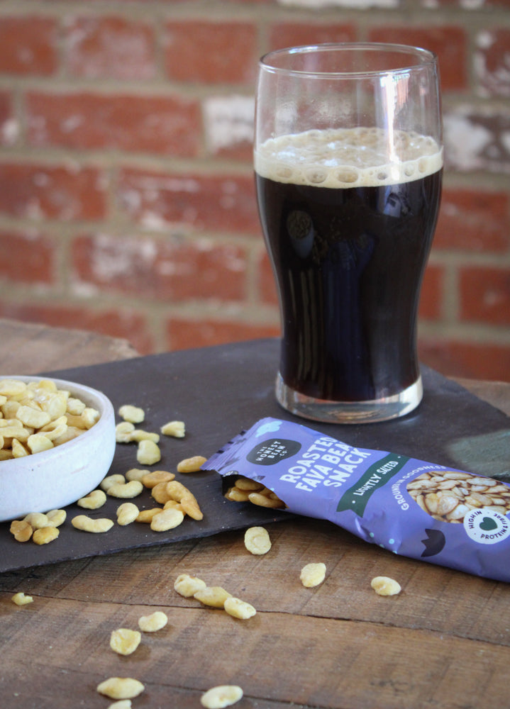 Lightly salted roasted fava bean snacks next to a pint glass of milk stout
